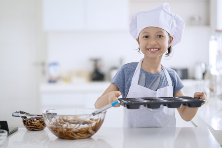 Portrait of cute little girl holding a mold with chocolate dough to make cookie and ready for baking in the kitchen at homeの写真素材