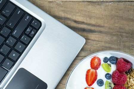 Business breakfast with a bowl of yogurt and laptop computer on the wooden desk in officeの写真素材
