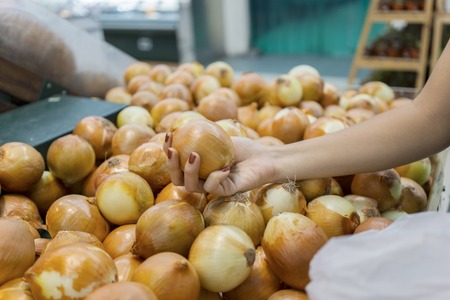 Closeup of young woman hand pick up onion on the basket in the supermarket