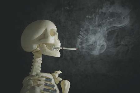 Image of a human skeleton with a cigarette in teeth. Shot with dark background