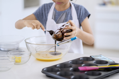 Closeup of little girl mixing eggs dough and chocolate to make cookie dough on the bowl in the...