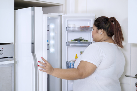 Picture of young fat woman checking foods in refrigerator while standing in the kitchenの写真素材