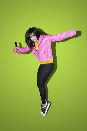 Pretty female dancer taking selfie photo while jumping with a mobile phone in the studio