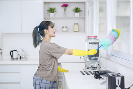 Portrait of pretty housewife is cleaning windows with a duster brush and standing in the kitchen