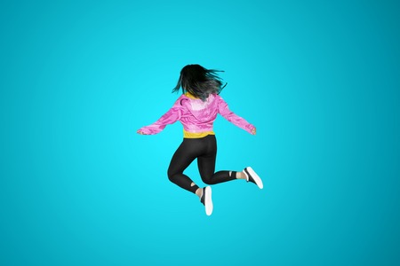 Back view of female modern dancer jumping in the studio with blue background