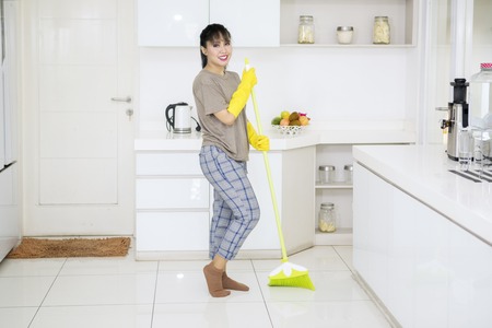 Picture of young housekeeper cleaning floors with a broom while standing in the kitchenの写真素材