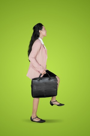 Portrait of pretty businesswoman carrying a suitcase while posing walk on the stairs in green screenの写真素材