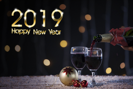 Image of an unknown woman pouring champagne into two glasses on the table with a text of 2019 Happy New Yearの写真素材