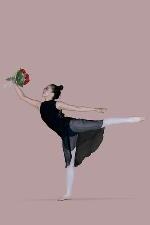 Picture of a young female ballet dancer is dancing in the studio with graceful poses while holding a...