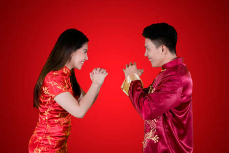 Image of young Chinese couple wearing cheongsam dress while congratulating each other. Shot in red backgroundの写真素材