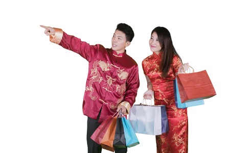 Chinese New Year Concept. Young Chinese couple holding shopping bags while pointing at something in the studioの写真素材