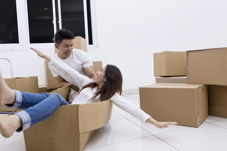 Picture of excited Asian couple is playing with a cardboard box while moving into a new houseの写真素材