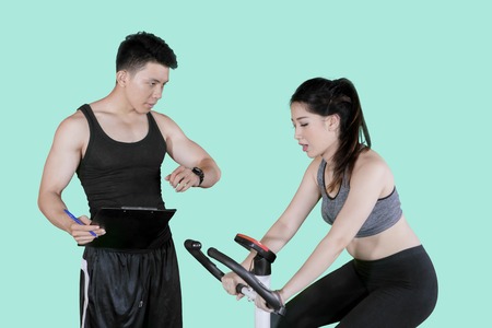 Picture of male trainer timing his client during uses exercise bike in the studioの写真素材