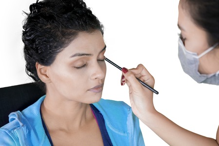 Picture of young makeup artist applies eyeshadow on her client face in the studio