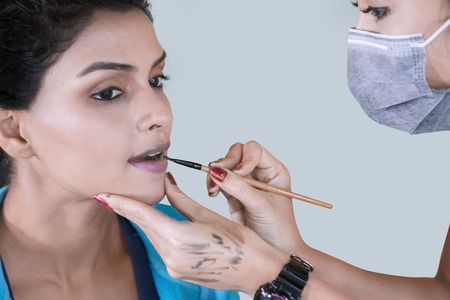 Picture of makeup artist applying a makeup brush on her client lips with lipstick in the studioの写真素材