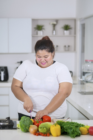 Picture of fat woman chopping vegetables while preparing meals in the kitchenの写真素材