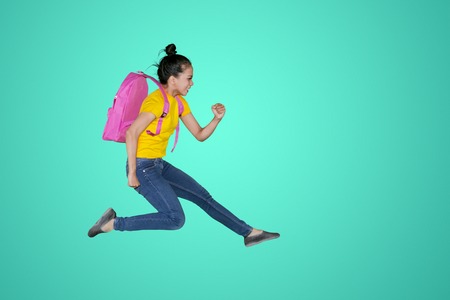 Side view of Asian female student carrying a backpack while running fast in the studio. Shot with green screenの写真素材