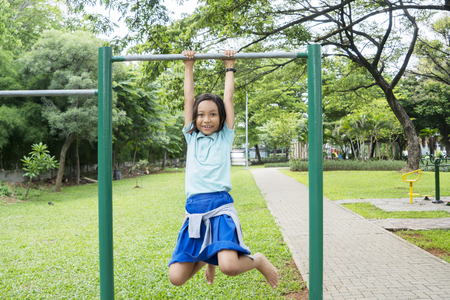 Picture of an Asian little girl hanging on a horizontal bar while playing in the playground