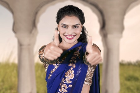 Picture of young Indian woman smiling at the camera while showing thumbs up at homeの写真素材