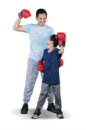 Full length of little boy wearing boxing gloves while standing with his father in the studio,...