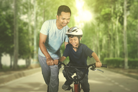Picture of a happy little boy learning to ride a bicycle with his father in the park. Shot at summer timeの写真素材
