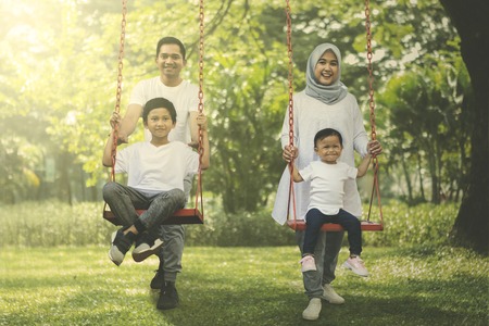 Portrait of happy Muslim family playing with swings in the park. Shot at summertimeの写真素材