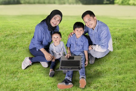 Top view of young parents and their children using a laptop while sitting together in the parkの写真素材