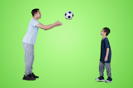 Picture of young man throwing a soccer ball to his son while playing in the studio with green screenの写真素材