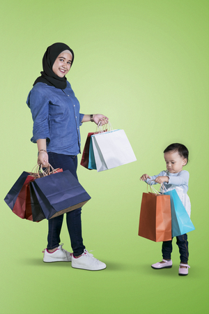 Beautiful woman carrying shopping bags while standing with her daughter in the studioの写真素材
