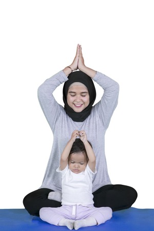 Portrait of young mother looks happy while doing yoga exercises with her daughter in the studio, isolated on white backgroundの写真素材