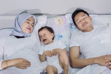 Top view of young tired parents sleeping with her cry daughter on the bed. Shot at midnightの写真素材