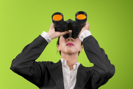 Low angle view of young businesswoman using binoculars while standing in the studio with green screenの写真素材