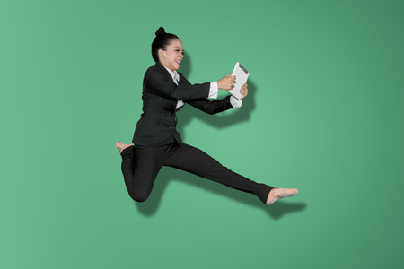 Asian businesswoman using a digital tablet while leaping in the studio with green screenの写真素材