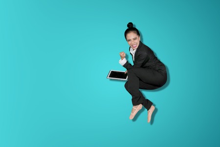 Happy business woman celebrating success by jumping in the studio while holding a digital tabletの写真素材