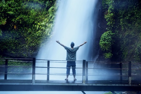 Rear view of young man standing on the suspension bridge while enjoying Situ Gunung waterfall view in Sukabumi, Indonesiaの写真素材