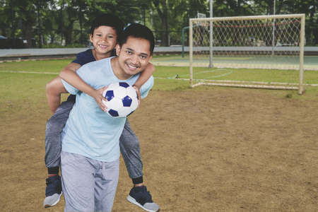 Picture of happy father piggybacking his son after playing football in the fieldの写真素材