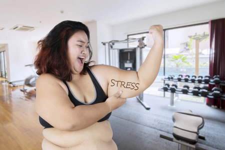 Picture of obese woman looks sad while showing her flabby bicep with stress word. Shot in the fitness centerの写真素材