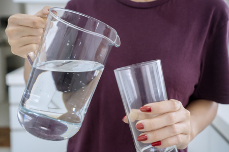 Close up of unknown woman holding a pitcher and glass while standing in the kitchen room