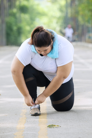 Picture of a young fat woman tying her shoelaces before doing run exercises on the roadの写真素材