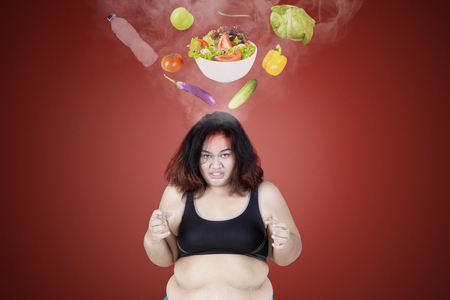 Picture of angry fat woman hating healthy food while standing under vegetables in the studioの写真素材