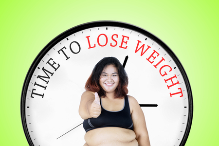 Happy fat woman showing her thumb up while standing with text of time to lose weight on a big clockの写真素材