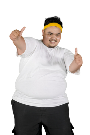 Portrait of overweight man showing thumbs up at the camera while standing in the studio, isolated on white backgroundの写真素材