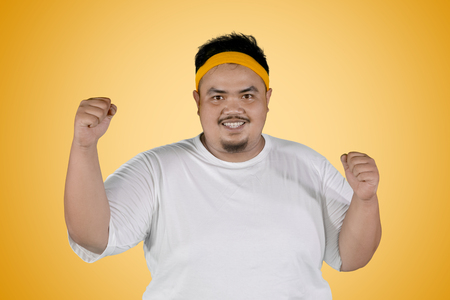 Picture of happy fat man expressing his success to lose weight while standing with yellow backgroundの写真素材