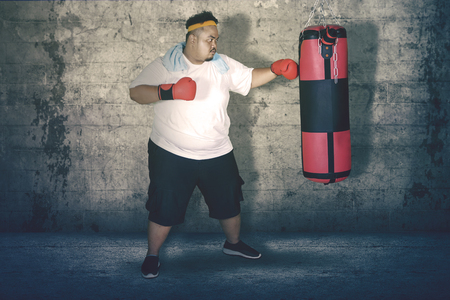 Picture of obese man punching a boxing bag and exercising in the studioの写真素材