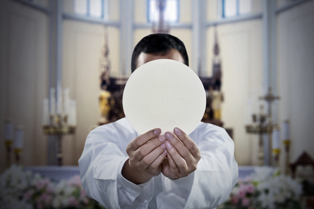 Picture of pastor celebrating a mass while holding a sacramental bread in the churchの写真素材