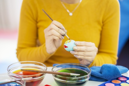 Close up of young woman hands decorating Easter eggs with liquid dye at homeの写真素材