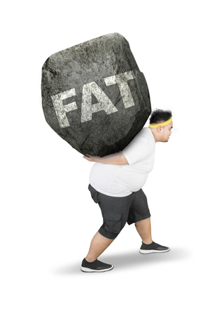 Side view of young obese man carrying fat word in a rock while walking in the studioの写真素材