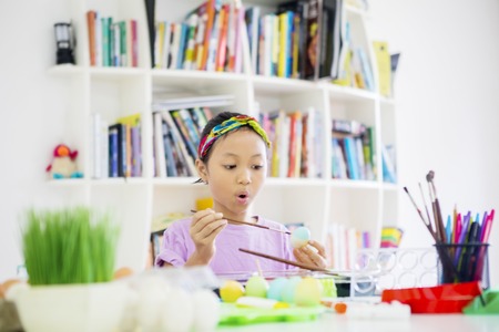 Picture of cute little girl looks shocked while painting eggs for Easter in the library