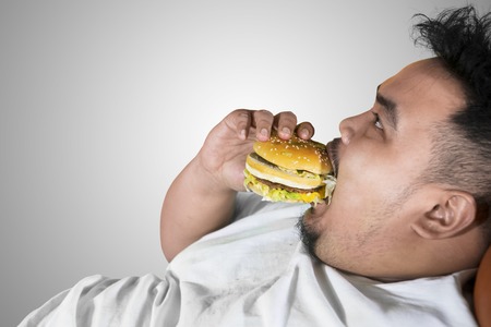 Close up of voracious fat man eating a burger, isolated on white backgroundの写真素材