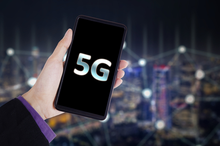 Internet speed concept. Close up of young businessman holding a mobile phone with 5G network symbolの写真素材